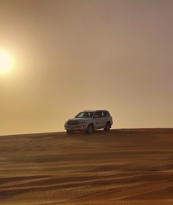 Home A white Toyota SUV parked on a sand dune in the Dubai desert during sunset.